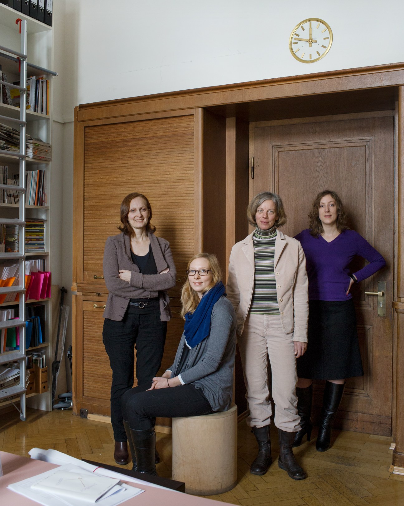 Five women pose together in an office with wooden cabinetry and bookshelves.