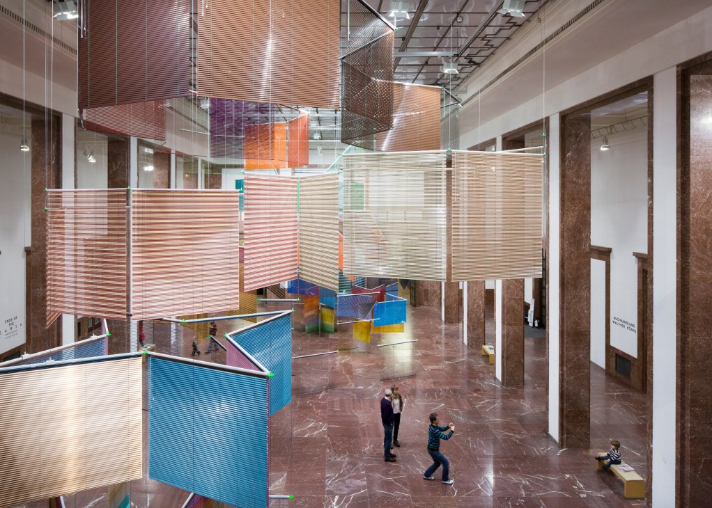Haegue Yang's colorful suspended Venetian blind installation in Haus der Kunst's Middle Hall with visitors below.
