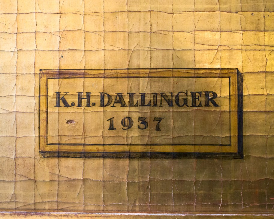 Engraved plaque reading 'K.H. DALLINGER 1937' on a cracked golden tile wall.