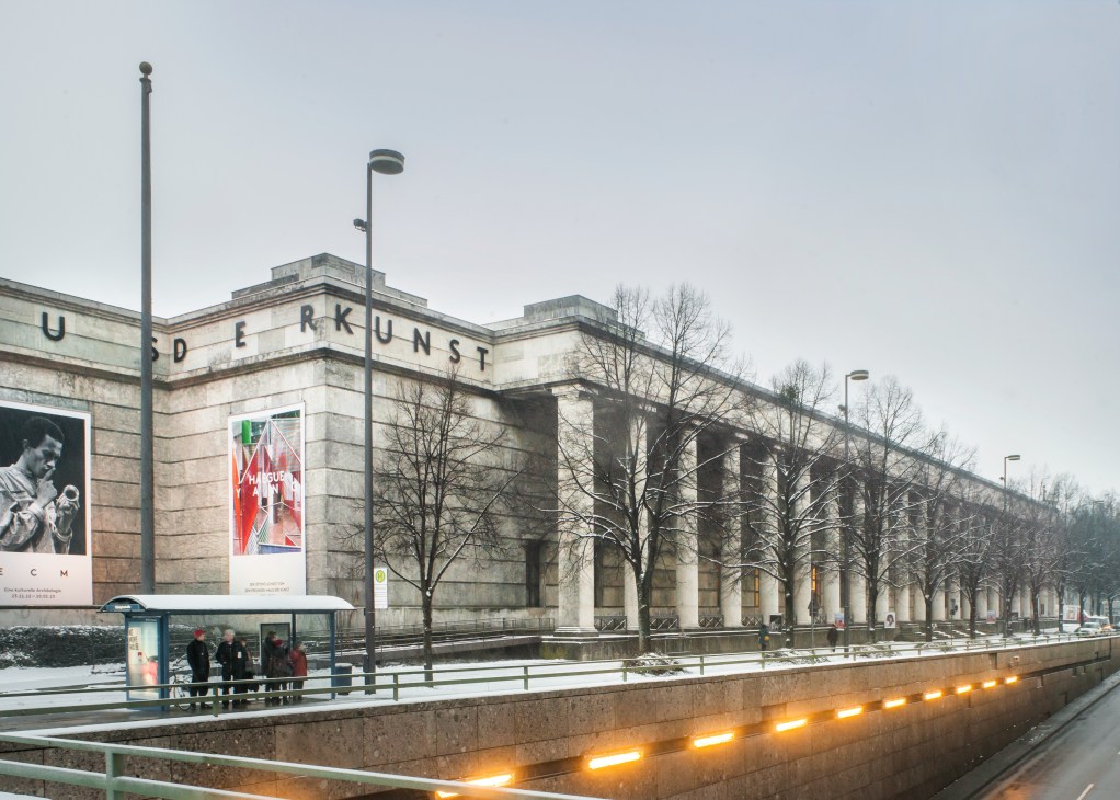 Exterior view of Haus der Kunst's neoclassical stone façade with colonnade of pillars and 'Haus der Kunst' text visible on the building.