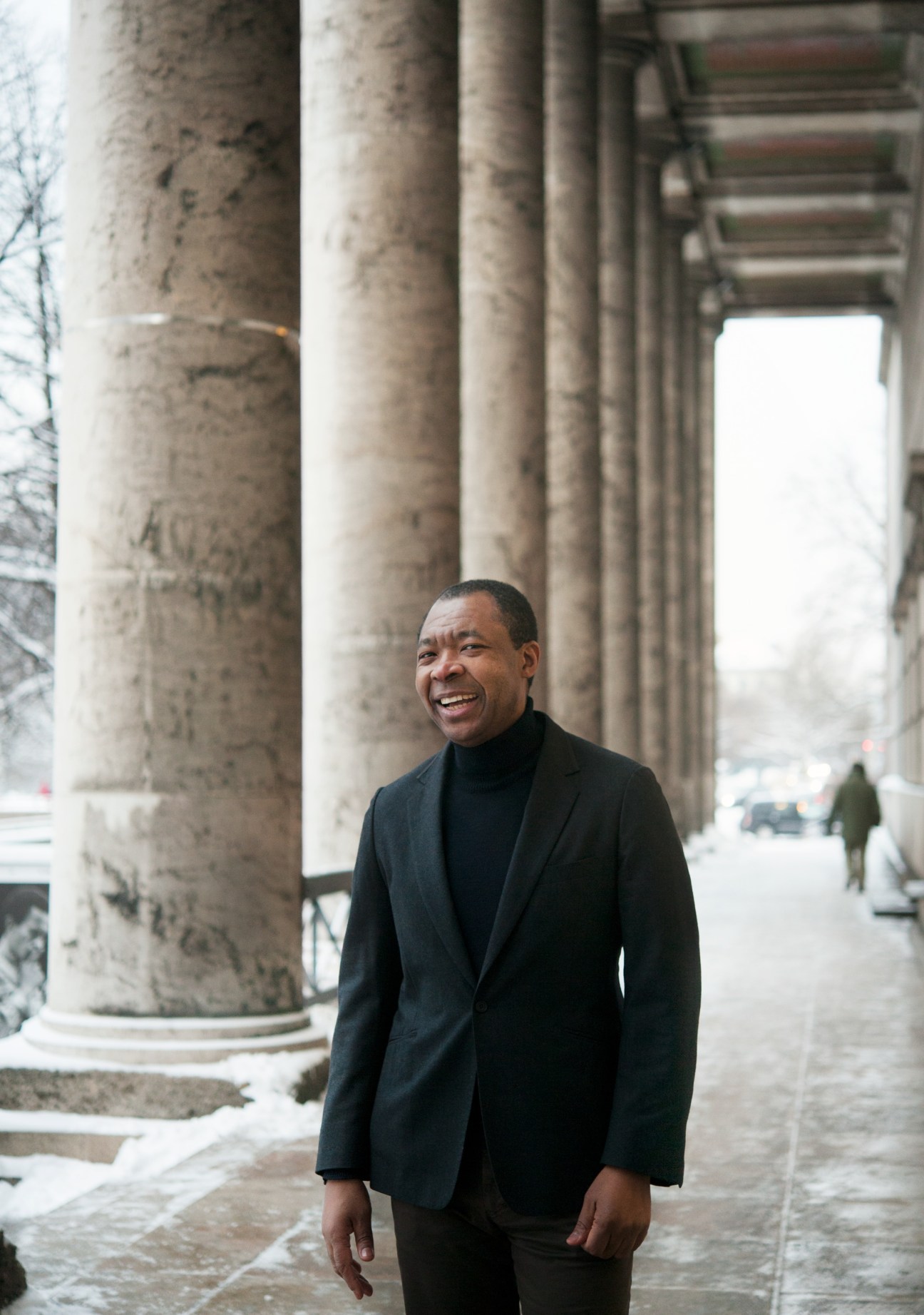 Okwui Enwezor, director of Haus der Kunst, stands smiling beneath the museum's neoclassical colonnade.