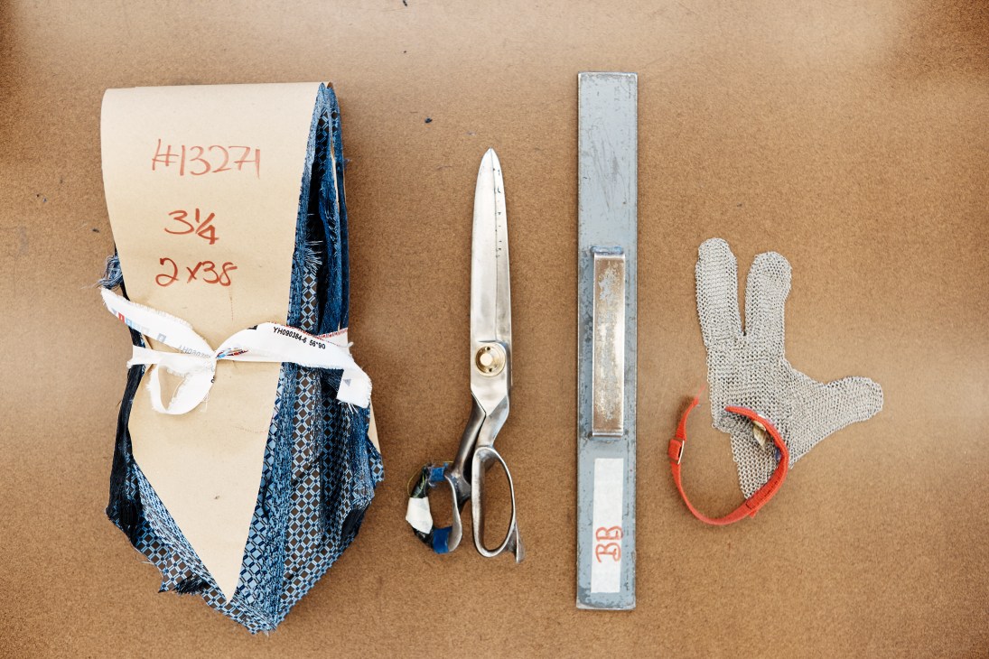 Tailor's tools including scissors, measuring tape, mesh glove, and fabric swatches arranged on brown surface.