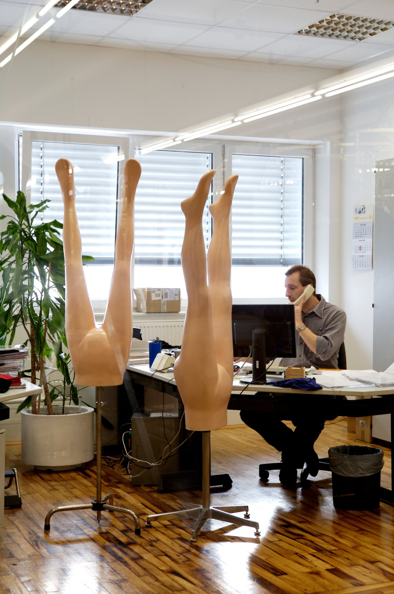 Worker printing Falke logo onto socks in factory office with mannequin legs.
