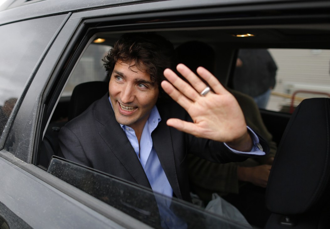 Man in dark suit and blue shirt waving from car window.