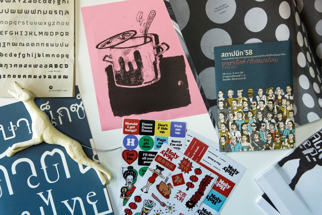 Collection of colorful design materials including pink illustration, typography samples, and stickers spread on table