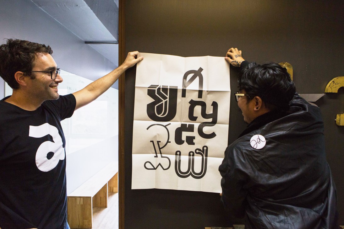 Two people at Farmgroup examining a large white poster with stylized black typography hanging on a wall