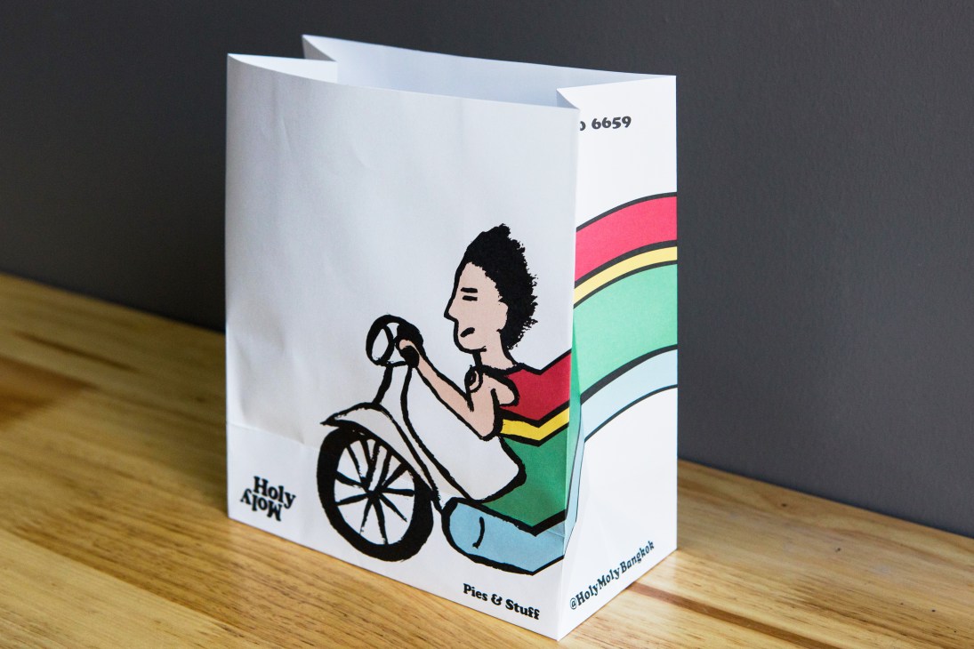 White paper bag with colorful illustrated design featuring person in wheelchair and rainbow stripes