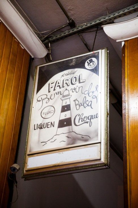 Hand-drawn sign in a framed window displaying O Farol's name and logos of tenant businesses including Fluxo, Líquen, Balsa and Choque.