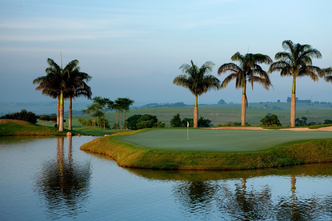 Golf course with manicured green surrounded by water, palm trees, and verdant landscape at Fasano Boa Vista.