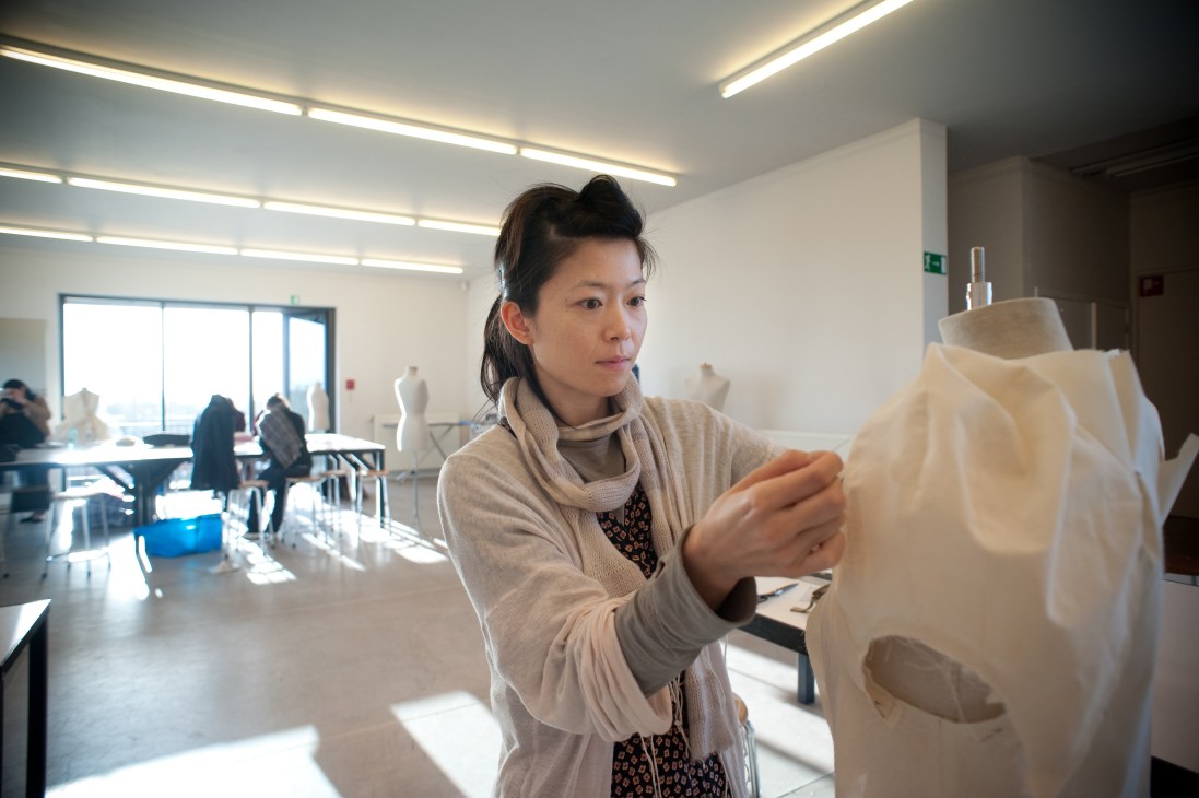 Student Huei-Hsua Sun examines a cream-colored fabric garment in a bright design studio.