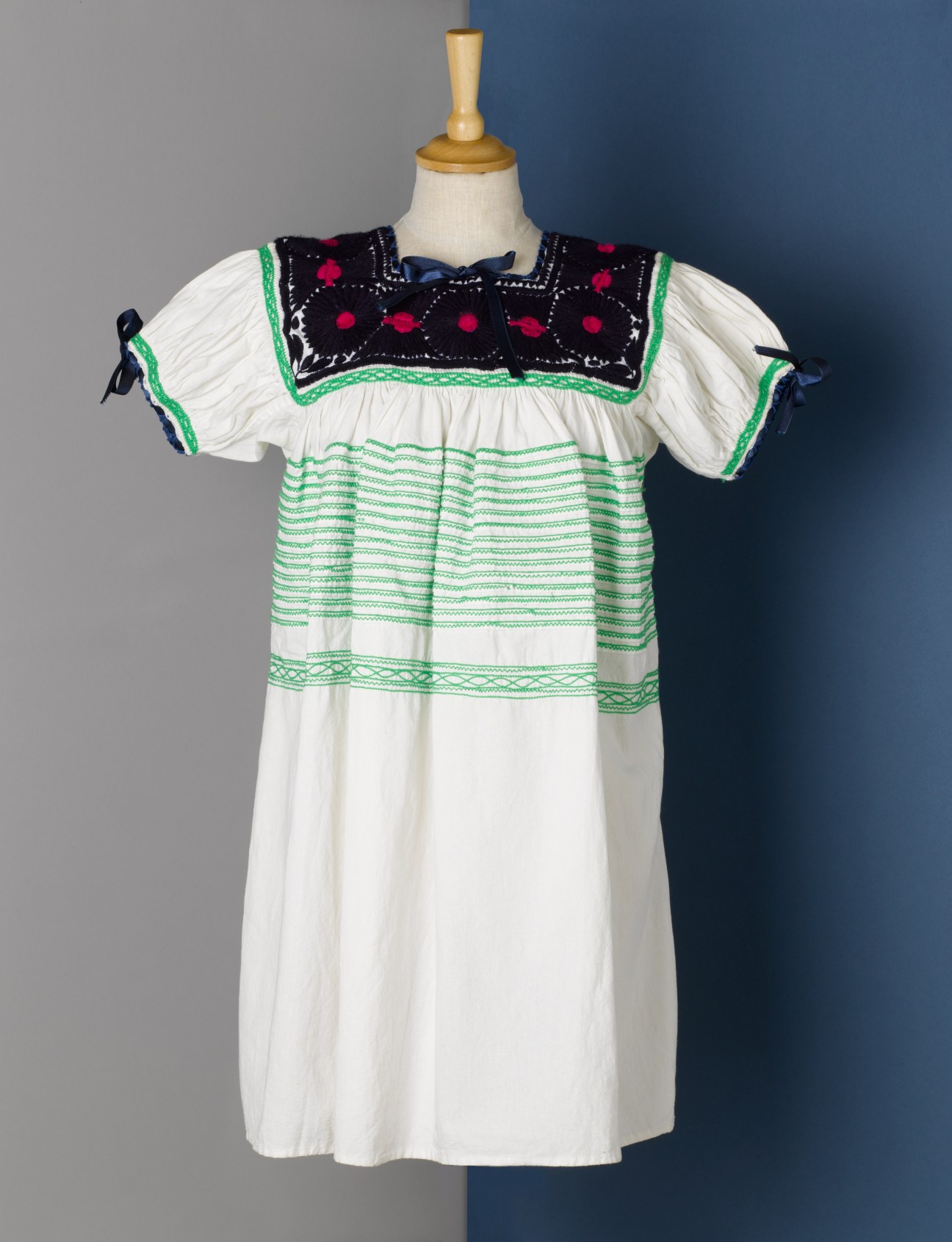 Hand-embroidered white cotton dress with green geometric patterns and black embellished neckline by Sacatinta.