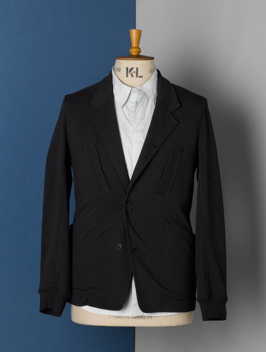 Black blazer with white shirt on dress form against blue and grey background.