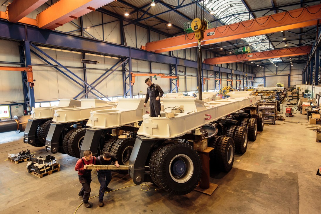 Workers assemble industrial transport vehicles with cream-colored bodies and large black tires in a Kirow factory in Leipzig.