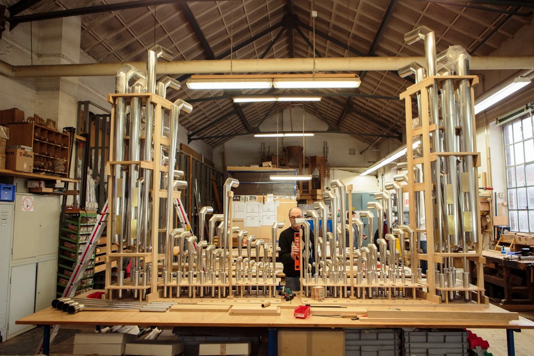 A craftsman works on a large wooden organ pipe frame in a workshop at Orgelbau Klais.