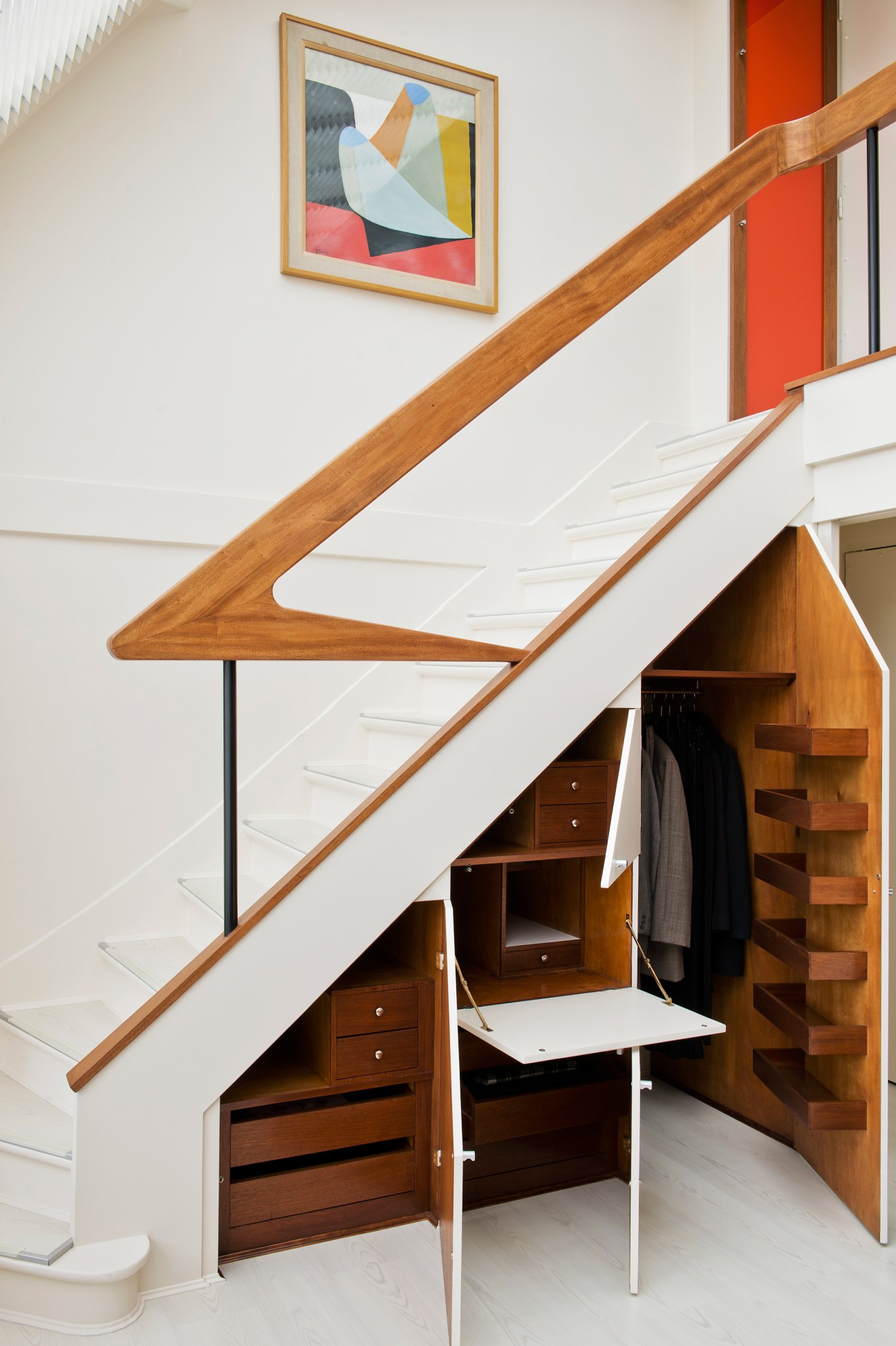 Mahogany staircase with open storage compartments underneath and abstract artwork on white wall above.