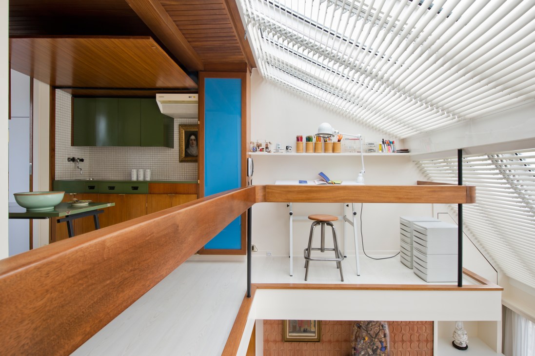 Modernist apartment upper floor with open kitchen featuring green cabinetry, mahogany counter, blue accent wall and white shelving.