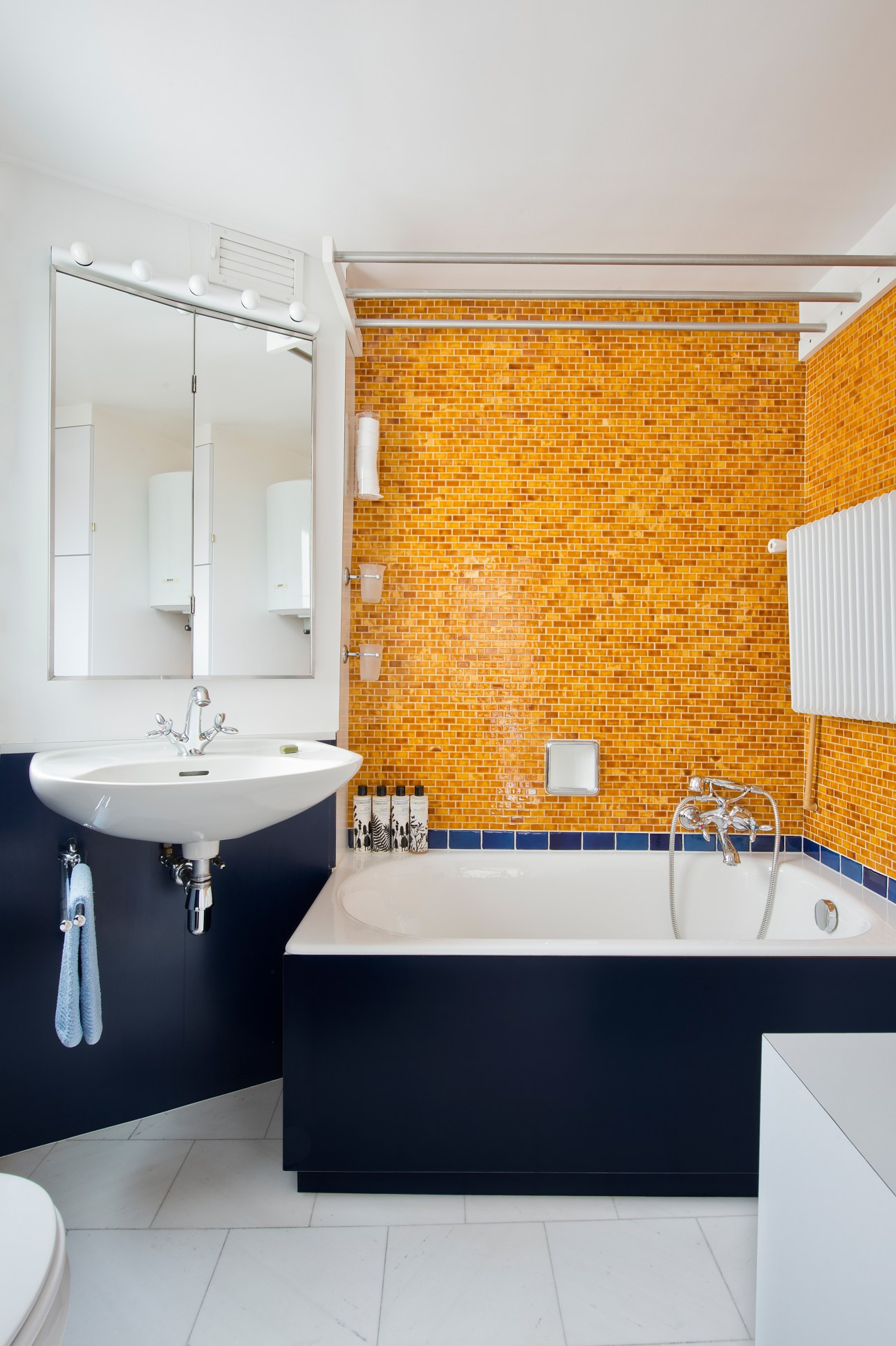 Bathroom with orange ceramic glass tile walls, white sink with mirror, dark vanity, and bathtub with blue tile accents.