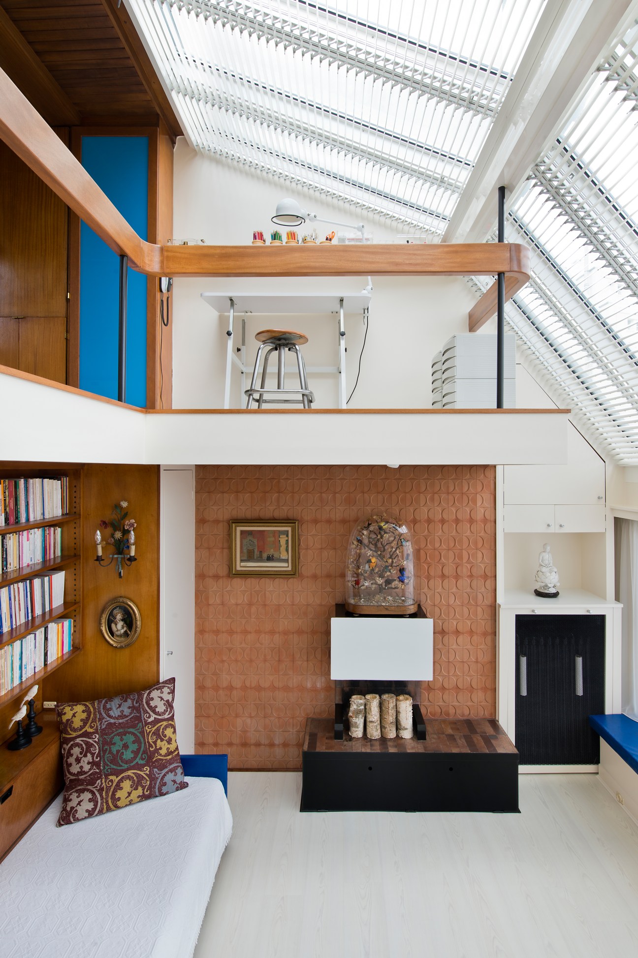 Modernist apartment interior with terracotta tile fireplace, mahogany shelving, mezzanine kitchen above and skylights.
