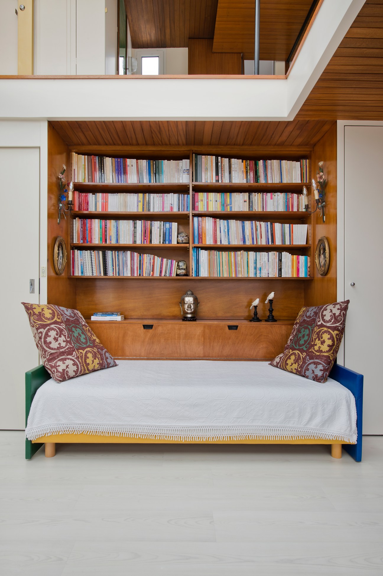 Mahogany sofa-bed with green and blue end panels, patterned cushions, and built-in bookshelf above.