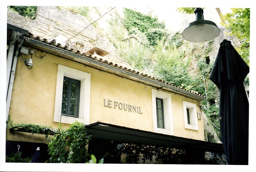 Le Fournil restaurant facade built into cliff rocks in Bonnieux, Provence with yellow ochre walls.