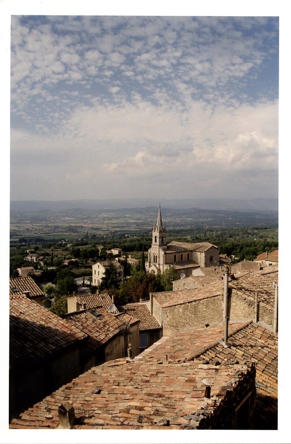 Aerial view of Bonnieux village with terracotta roofs, a church steeple, and the Luberon valley landscape below.