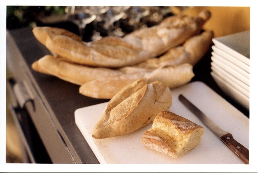 Fresh French baguettes and bread rolls on a white plate with a knife.