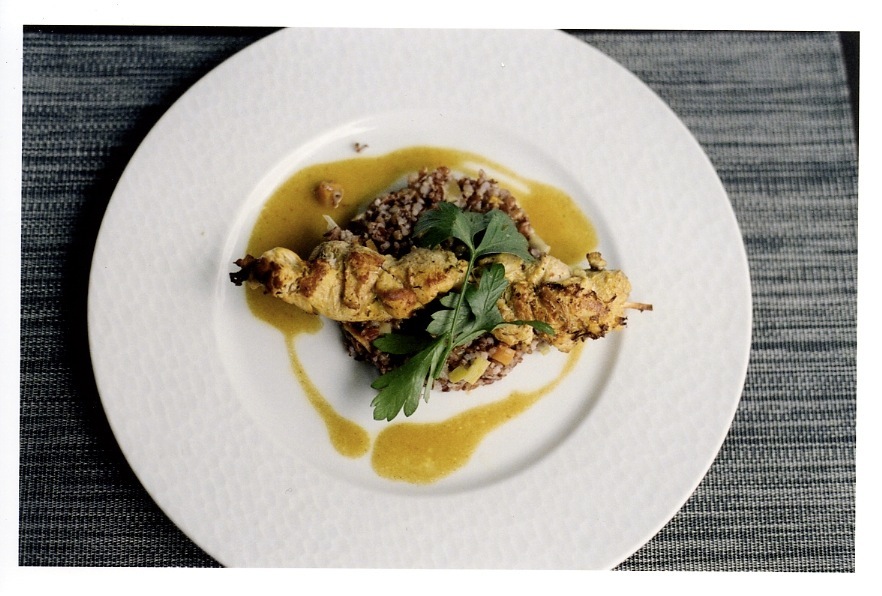 Brochette de volaille chicken kebab with spiced sauce, rice and herbs on white plate.