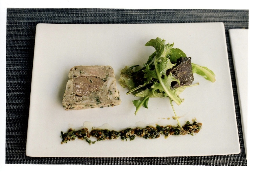 Presse de porc pâté with salad greens and herb garnish on a white plate.