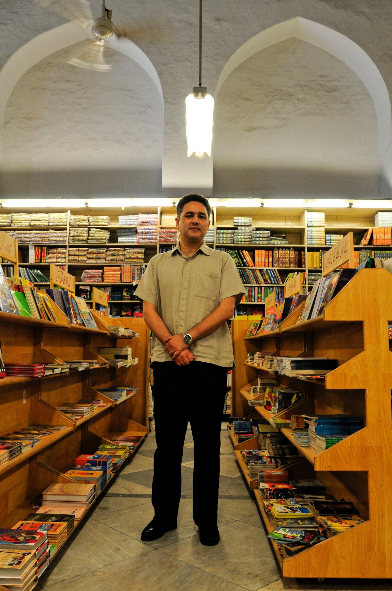Man standing in Ferozsons bookshop aisle with wooden shelves of books on either side.