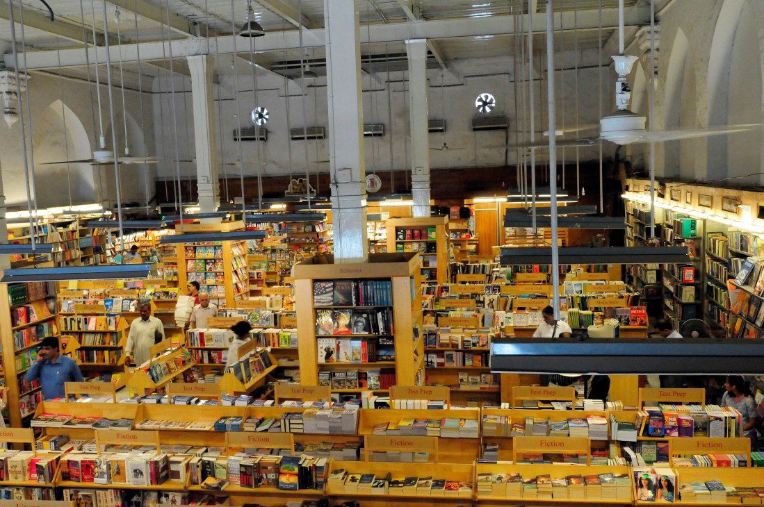 Interior of Ferozsons bookshop with high ceilings, yellow wooden shelves filled with books, and customers browsing.