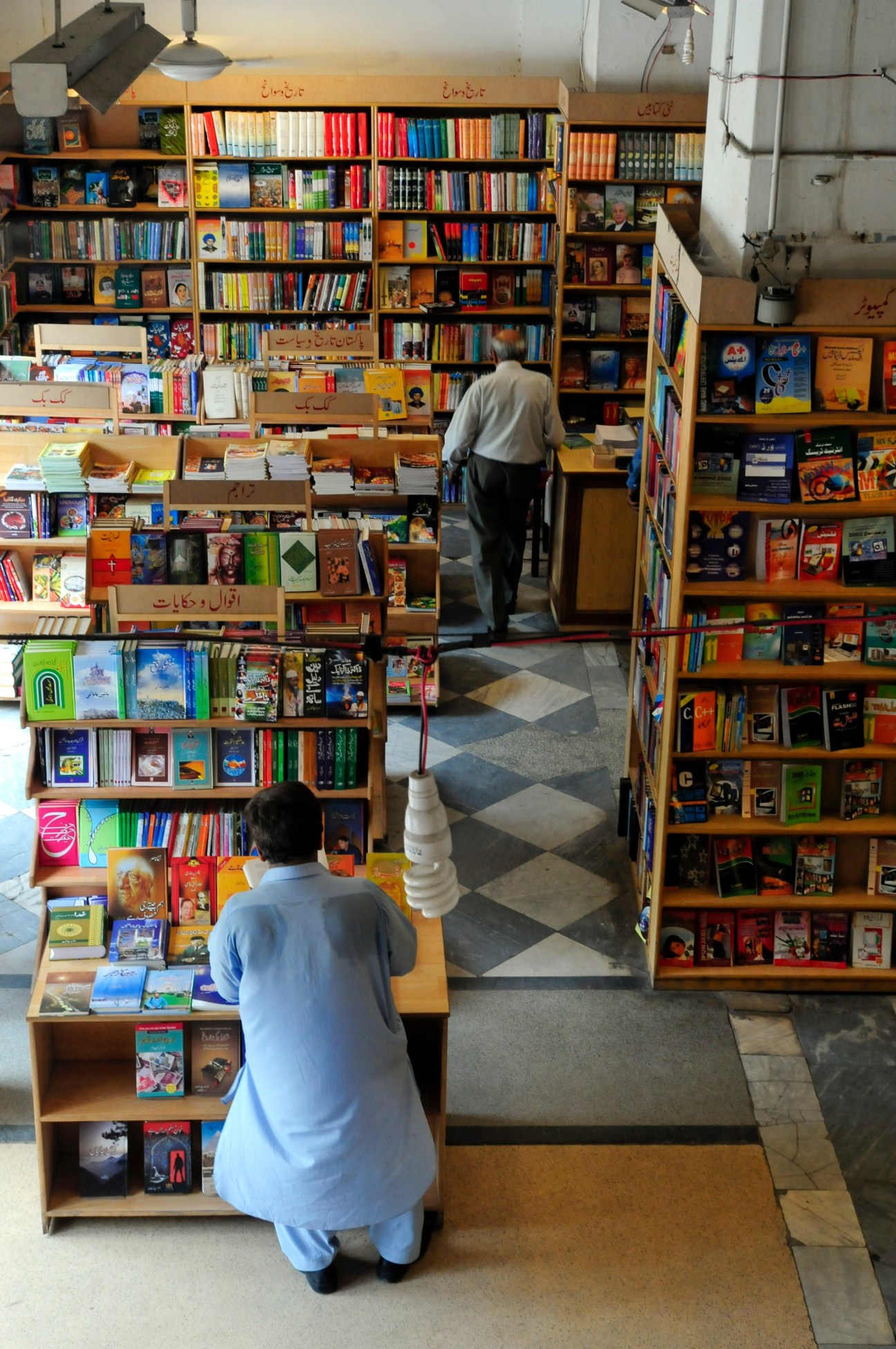 Interior view of Ferozsons Bookshop in Lahore with customers browsing shelves of colorful books and Urdu text signage.