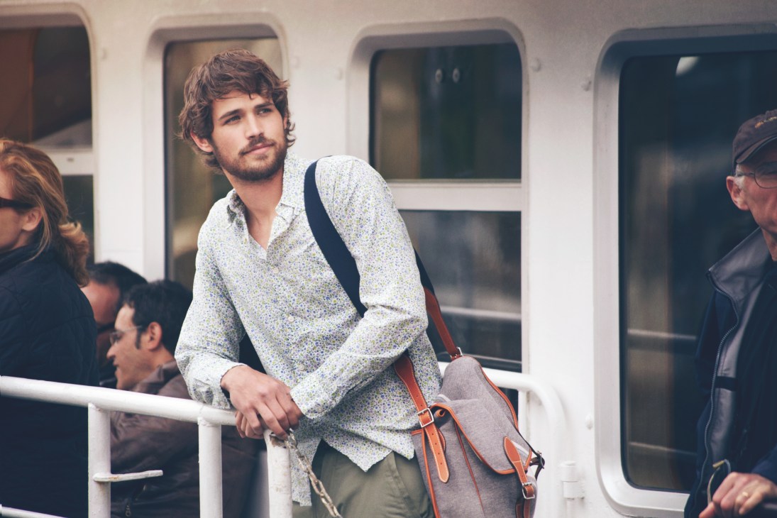 Man on ferry wearing patterned shirt and trousers with brown leather bag across shoulder