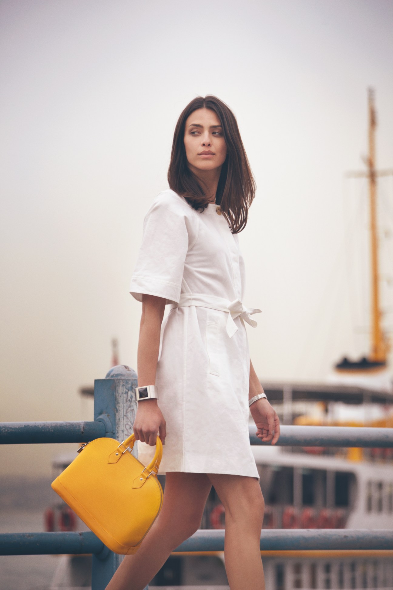 Woman in white Loewe dress with yellow Louis Vuitton bag on ferry with sailboats in background