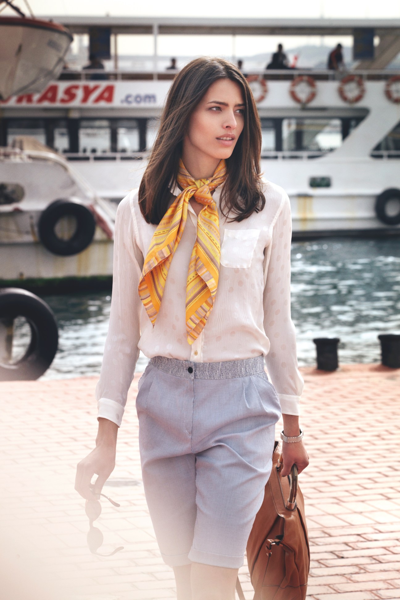 Woman in white shirt and lavender shorts with yellow scarf on Bosphorus ferry dock.