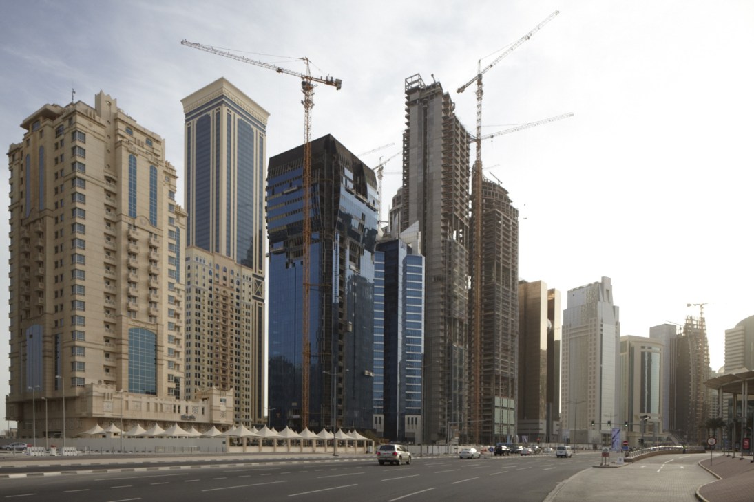 Wide street in downtown Doha lined with tall office and residential buildings under construction with cranes.