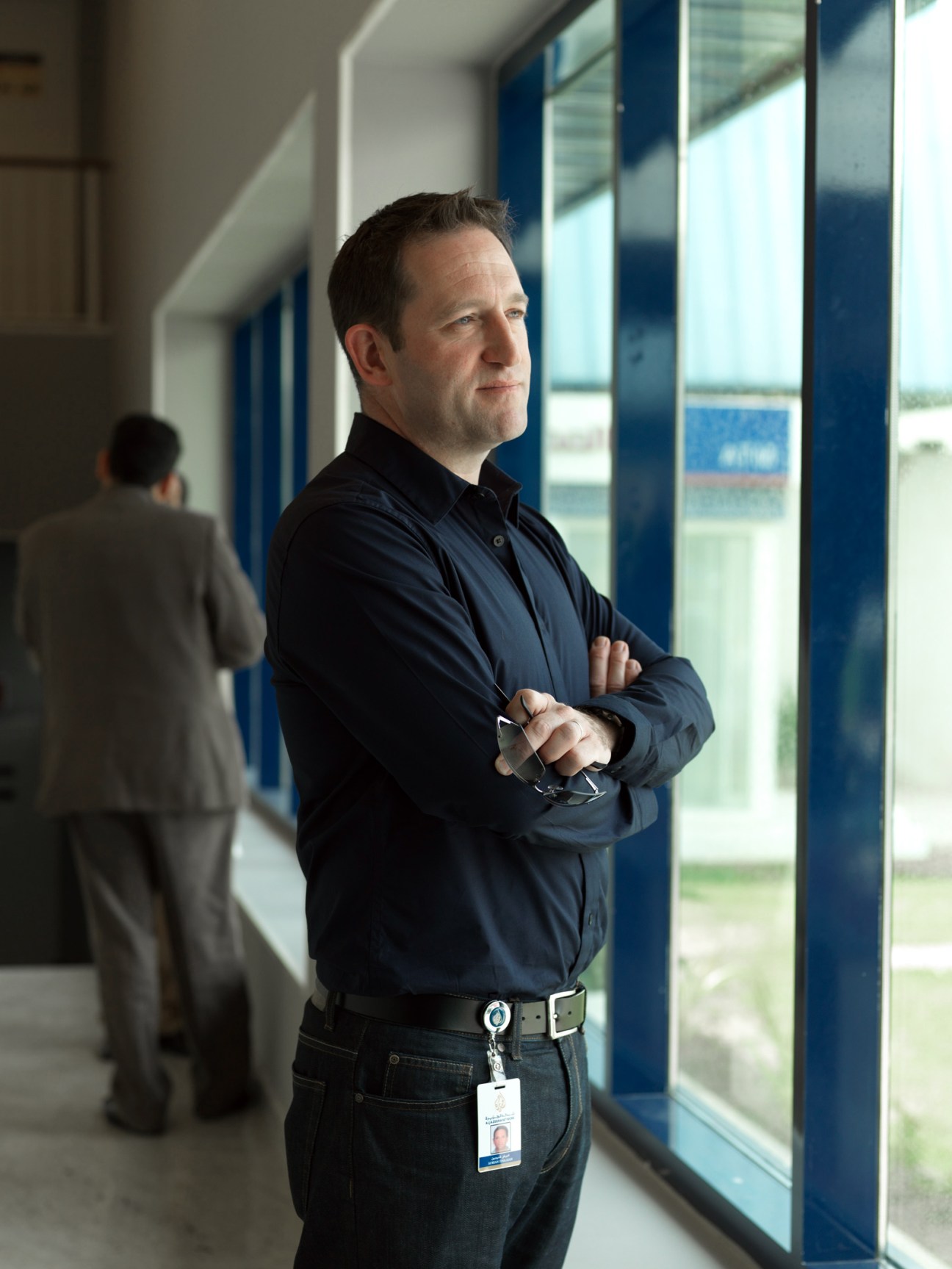 Adrian Finighan, a former BBC and CNN anchor, stands in a corridor at Al Jazeera English wearing a dark blue shirt and ID badge.