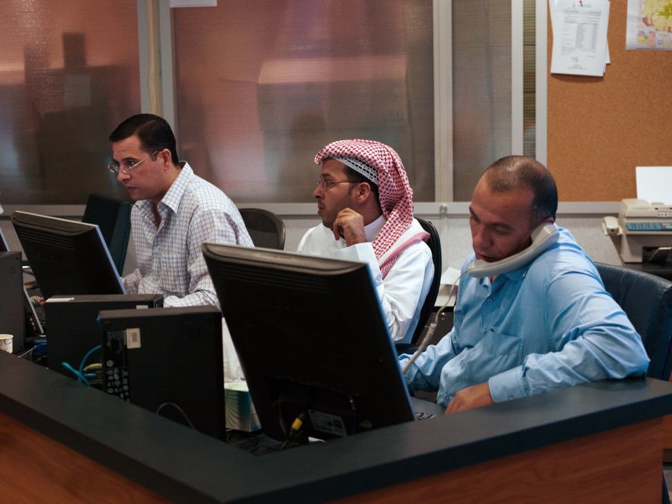 Three male editors at Al Jazeera Arabic newsroom working at computer terminals.