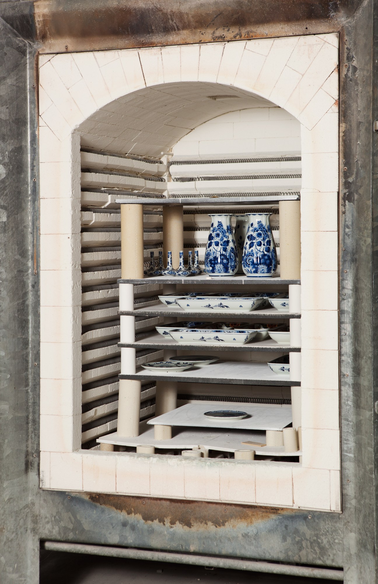 Blue and white ceramic vessels and plates arranged on shelves inside a kiln at Royal Delft pottery factory.