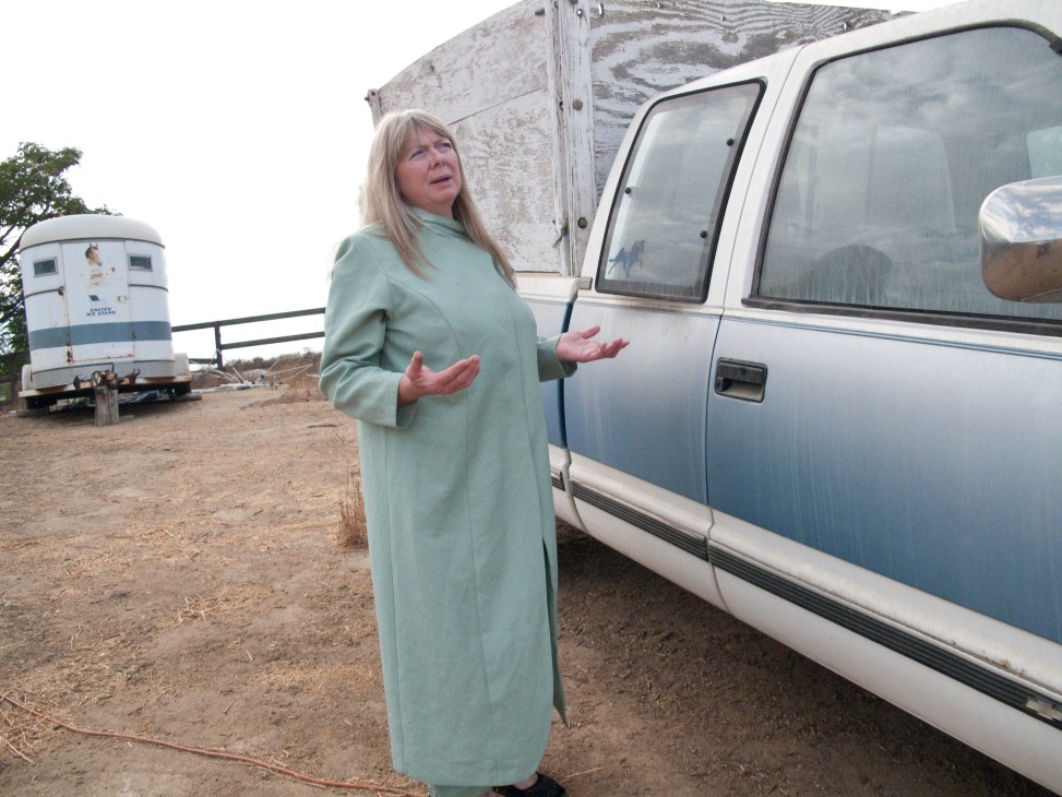 Woman in green coat standing beside vintage pickup truck at desert location