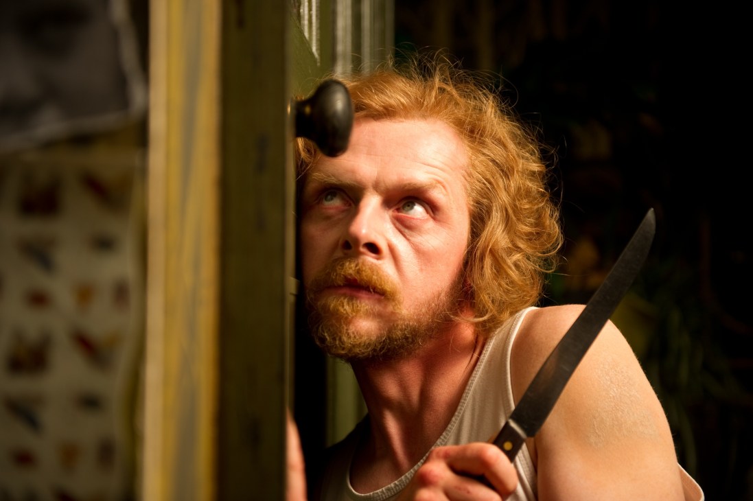 A man with reddish hair and beard wearing headphones around his neck, holding a knife, with an anxious expression.