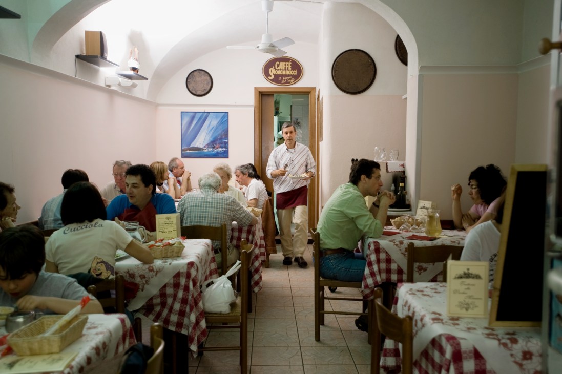 Interior of a casual Italian restaurant with diners seated at tables with red and white checkered tablecloths.