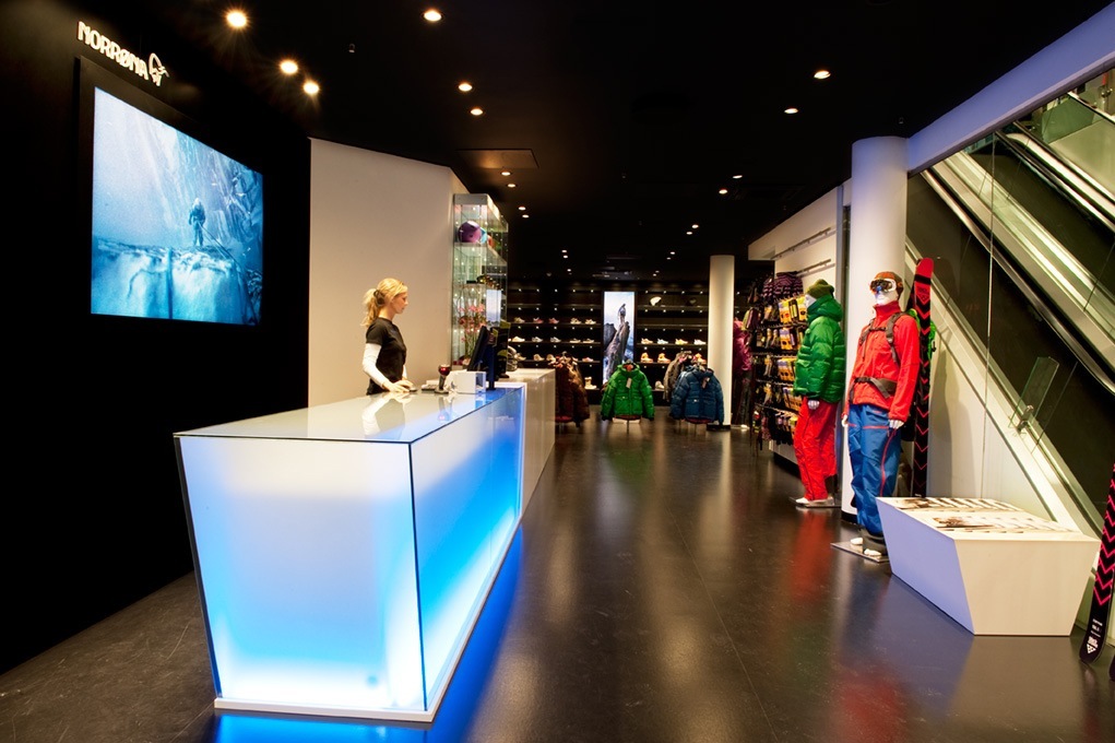 Norrøna retail store interior with illuminated counter, colorful outerwear displays, and video screen.