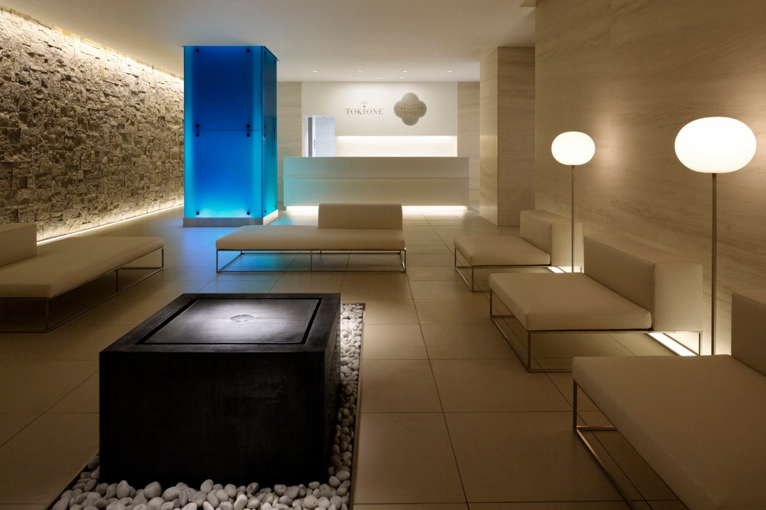 Modern spa reception area with stone walls, blue illuminated water feature, and minimalist furniture at Tokyo Station Hotel's Spa Tokione.