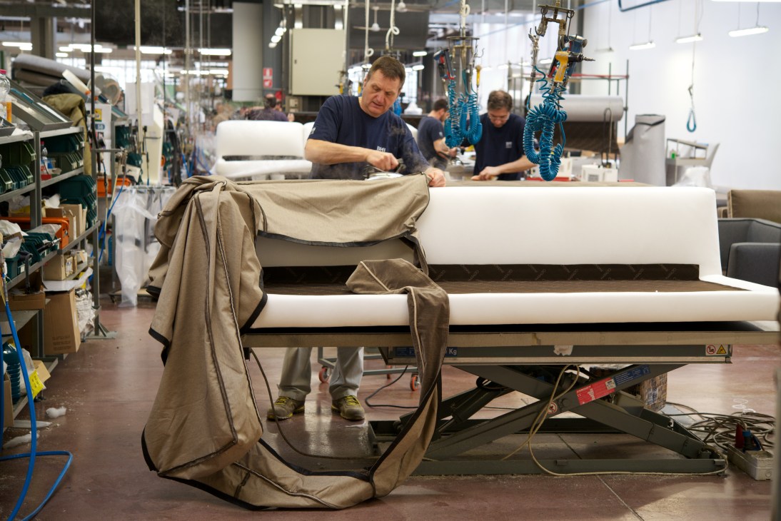 Worker fitting fabric cover onto a B&B Italia sofa frame in the upholstery department.
