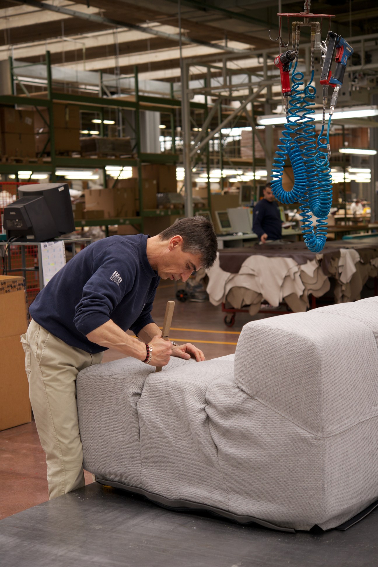 Worker fitting fabric cover onto a light grey upholstered sofa at B&B Italia factory.