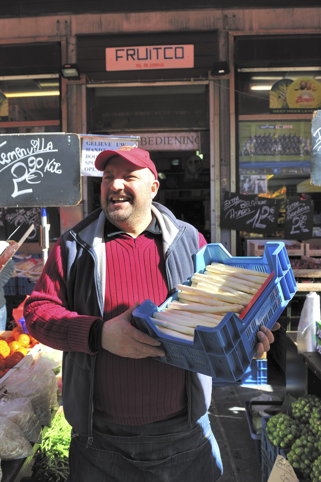 Bayram Özdemir, owner of Fruitco fruit and vegetable shop in Ghent, holding a blue crate of leeks outside his store.