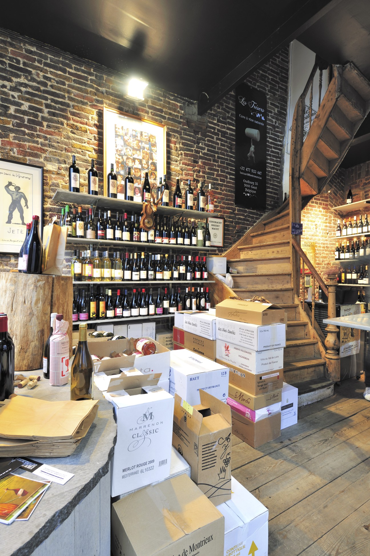 Les Trésors wine shop interior with shelves of natural wines, wooden stairs, and cardboard boxes on the floor.