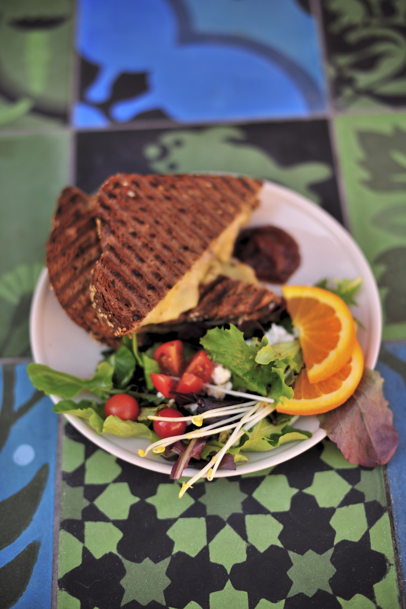 A croque sandwich with melted cheese and ham on a white plate with fresh salad and orange slices on a patterned placemat at Simon Says café.