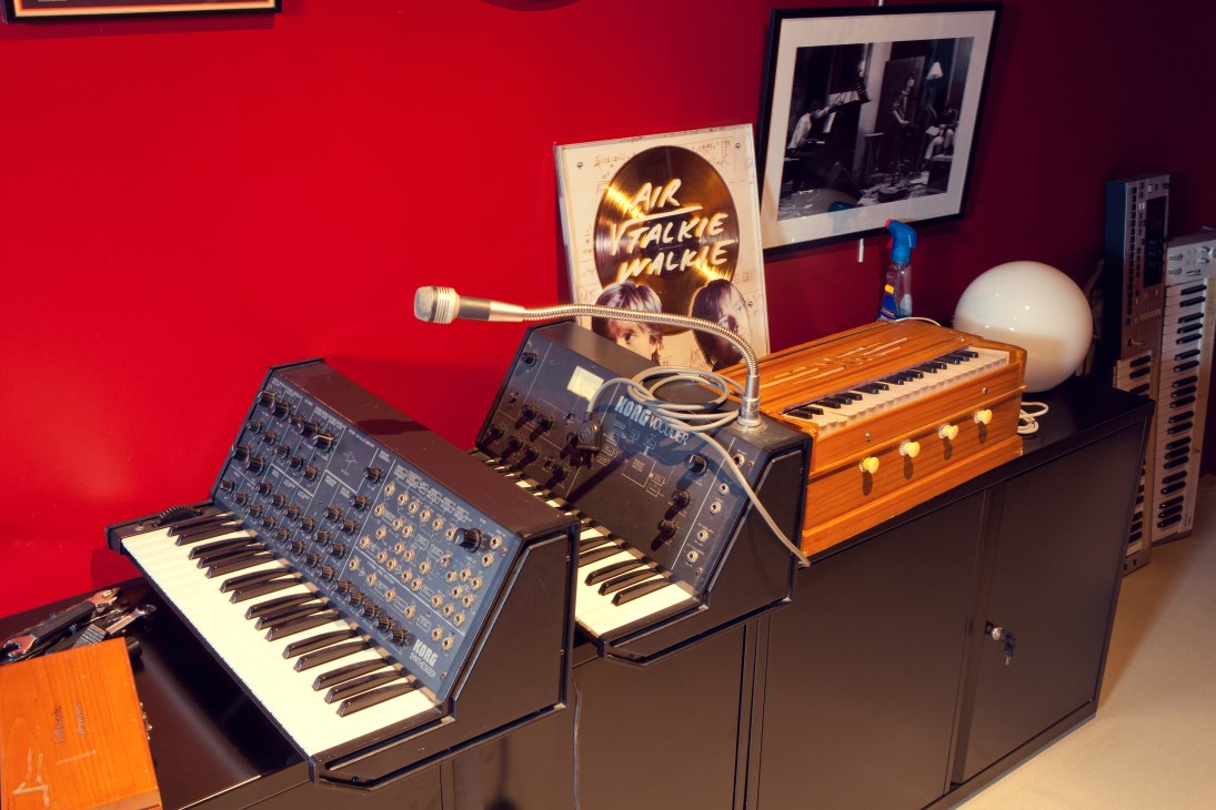 Vintage synthesizers and keyboards displayed against a red wall in Air's Atlas studio with gold records and framed photographs.