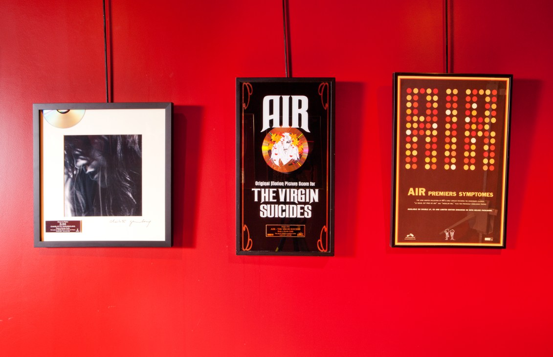 Three framed Air album artworks displayed on a red wall, including The Virgin Suicides soundtrack gold disc.